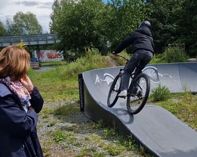 Radfahrer auf schwarzem Parcours, im Vordergrund eine Frau von hinten