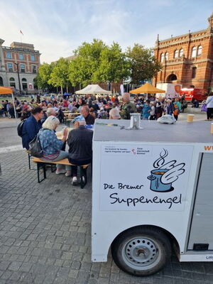 Anhänger, im Hintergrund viele Menschen an Tischen