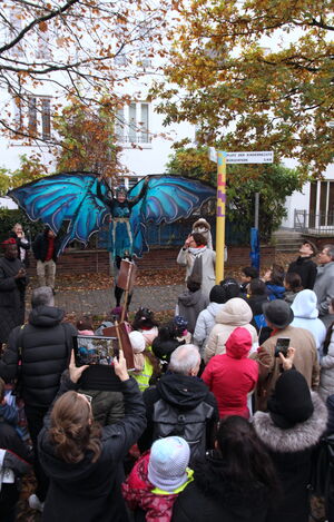 Viele Menschen, eine Stele "Platz der Kinderrechte Gröpelingen" und ein Mensch als großer Schmetterling verkleidet