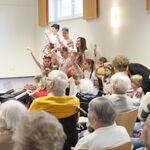 Ukrainische Kinder, mit Blumenkränzen, im Vordergrund Senior*innen als Zuschauer