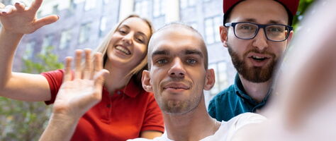 Drei junge Menschen winken lächelnd in die Kamera