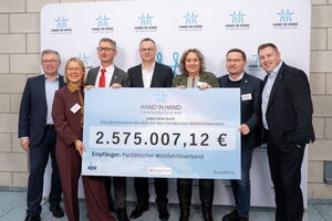 7 Personen in Anzügen halten einen großen Scheck über 2,757 Mio. Euro in der Hand