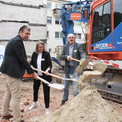 2 Männer un eine Frau mit Spaten auf Baustelle