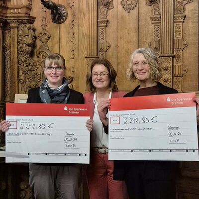 3 Frauen, 2 halten einen großen Scheck der Sparkasse in die Kamera